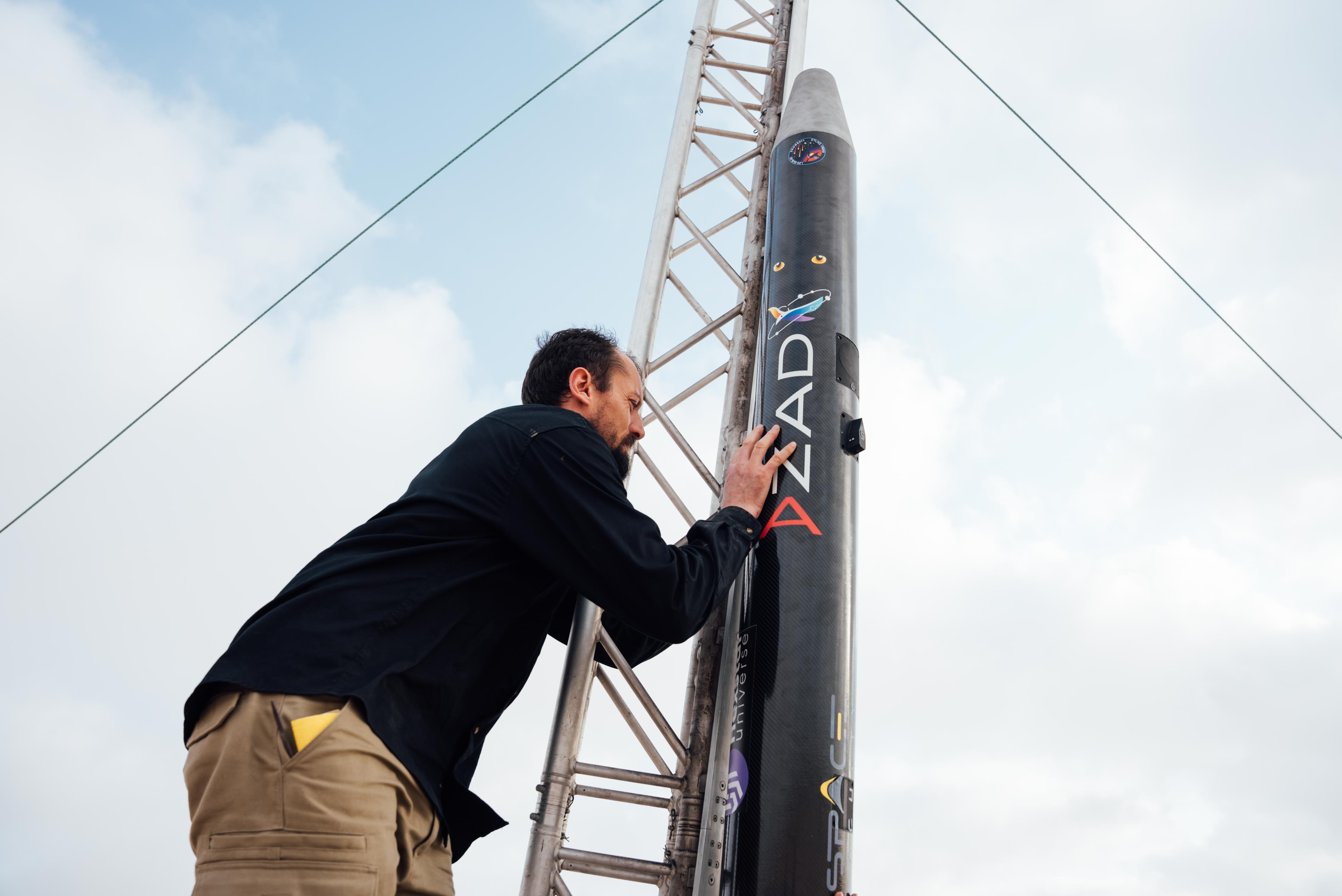 A crew member with a hand on the carbon airframe of Azad The Dreamer